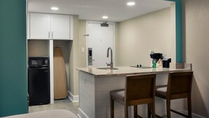 A compact kitchen with white cabinets, a microwave, a sink, and two wooden chairs. - Cozy North Ocean View Efficiency Vista 4th Floor (Myrtle Beach)