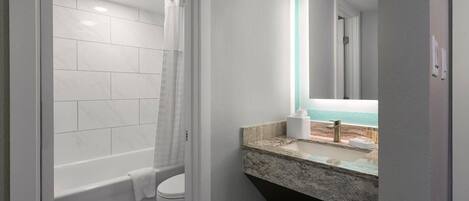 A bathroom with a bathtub, toilet, and a sink with a marble countertop.