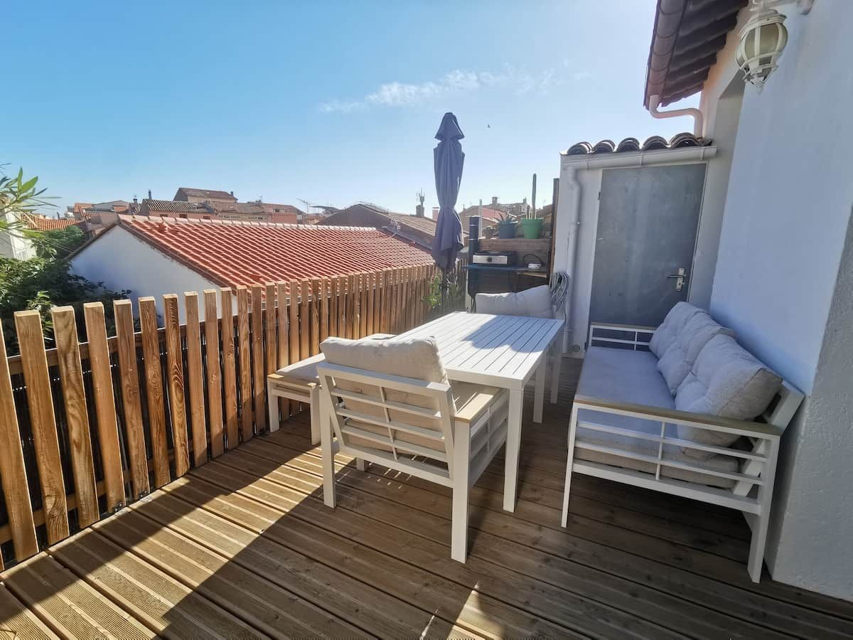 Una terraza de madera con una mesa, sillas, un sofá y vistas de los edificios circundantes.