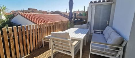Una terraza de madera con una mesa, sillas, un sofá y vistas de los edificios circundantes.