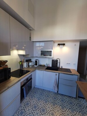 A compact kitchen with a microwave, toaster, kettle, and a sink.