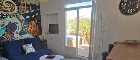 Una sala de estar con sofá, una mesita redonda, televisor y un comedor con mesa y sillas.
