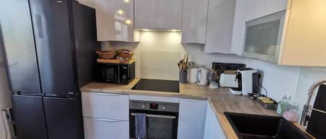 Een compacte keuken met een zwarte koelkast, een inbouwoven en een spoelbak.