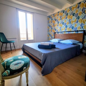 A bedroom with a bed, a chair, a window, and a patterned wall.
