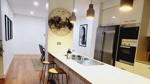 Una cocina moderna con una isla central, taburetes de bar, electrodomésticos de acero inoxidable, iluminación colgante y una gran obra de arte en la pared.