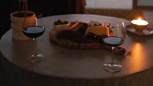 Una mesa con copas de vino y una vela, frente a una ventana con vistas a la ciudad.