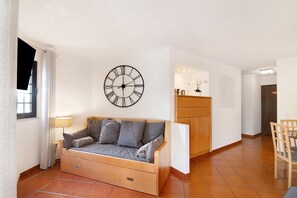 Ein Wohnzimmer mit Sofa, Wanduhr, Lampe, Esstisch und Küchenzeile.