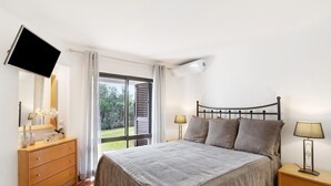 Une chambre à coucher comprenant un lit, une télévision, une commode, une table de chevet et une fenêtre donnant sur un paysage verdoyant.