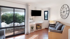 Un salon équipé d’un téléviseur, d’une cheminée, d’un canapé et d’une grande fenêtre donnant sur un espace verdoyant.