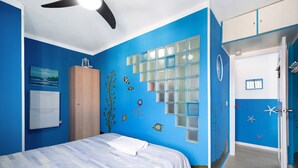 Una habitación con una cama, un armario, una puerta con ventanal y una pared con un mural azul.