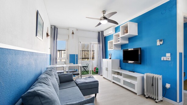 Un salón con un sofá gris, un mueble blanco para el entretenimiento, un ventilador de techo y un televisor.