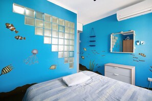 Una camera da letto con un letto, una cassettiera, uno specchio e un murale a tema oceano in blu.