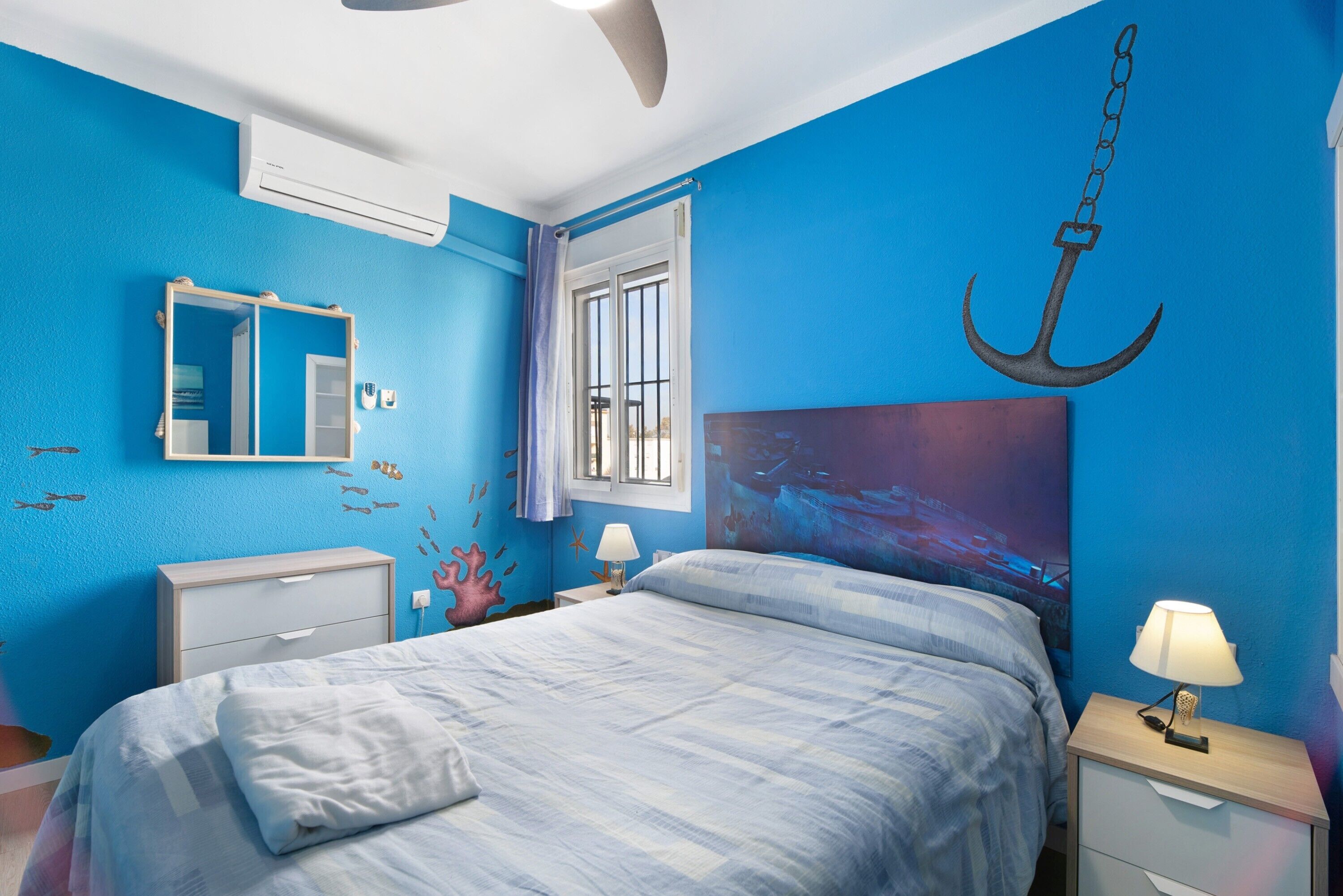 A bedroom with a bed, nightstands, a mirror, and a wall with a nautical theme.