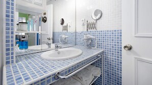 Un baño con un lavamanos blanco, un espejo, un perchero para toallas y una zona de ducha.