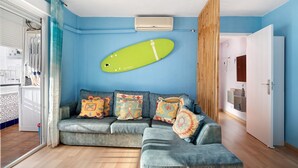 Une pièce avec un canapé d’angle gris, une planche de surf verte et une porte blanche.
