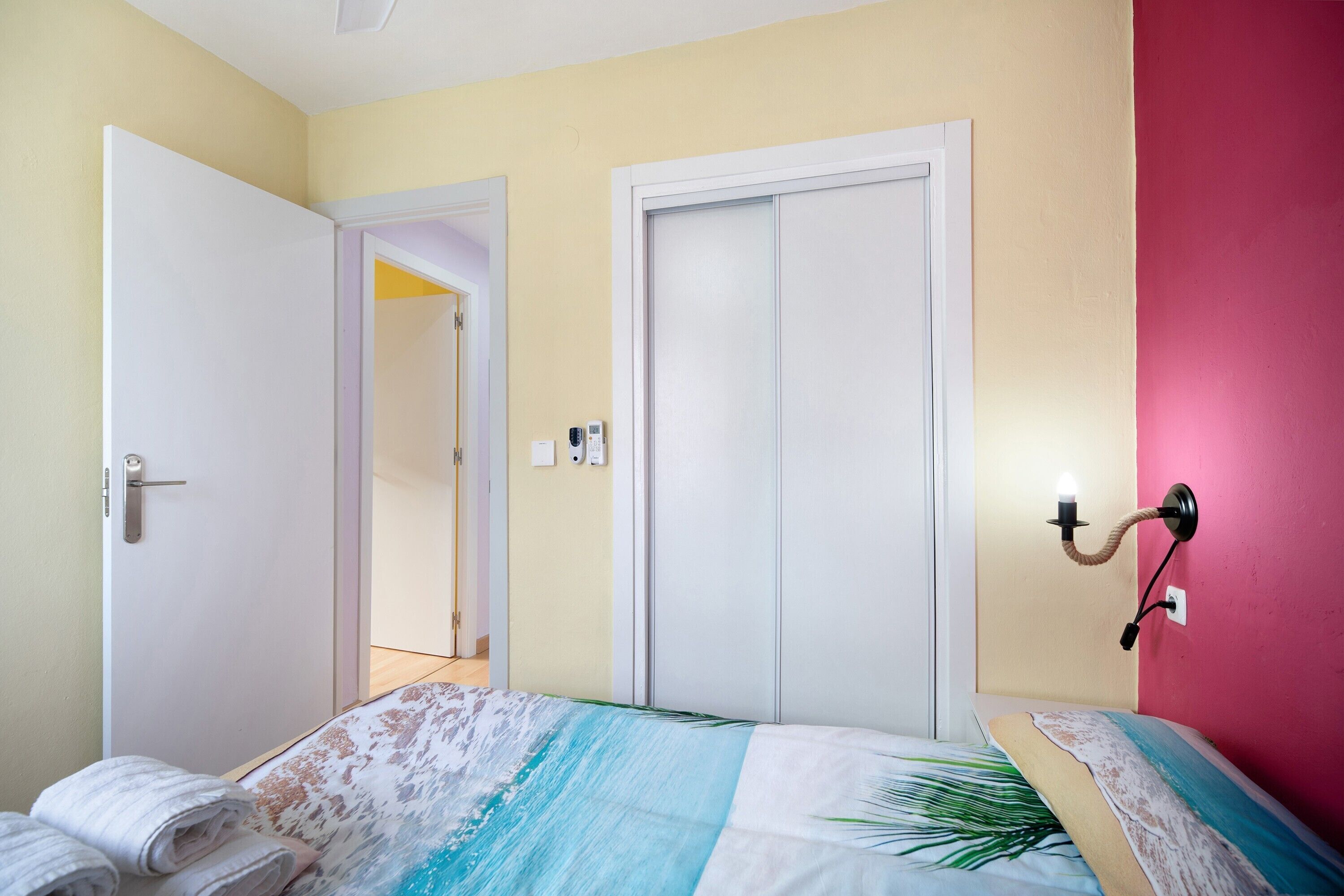 A bedroom with a bed, a door, and a wall-mounted light fixture.