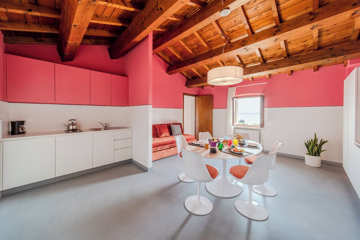 A modern kitchen with white cabinets, a wooden ceiling, and a pink wall.