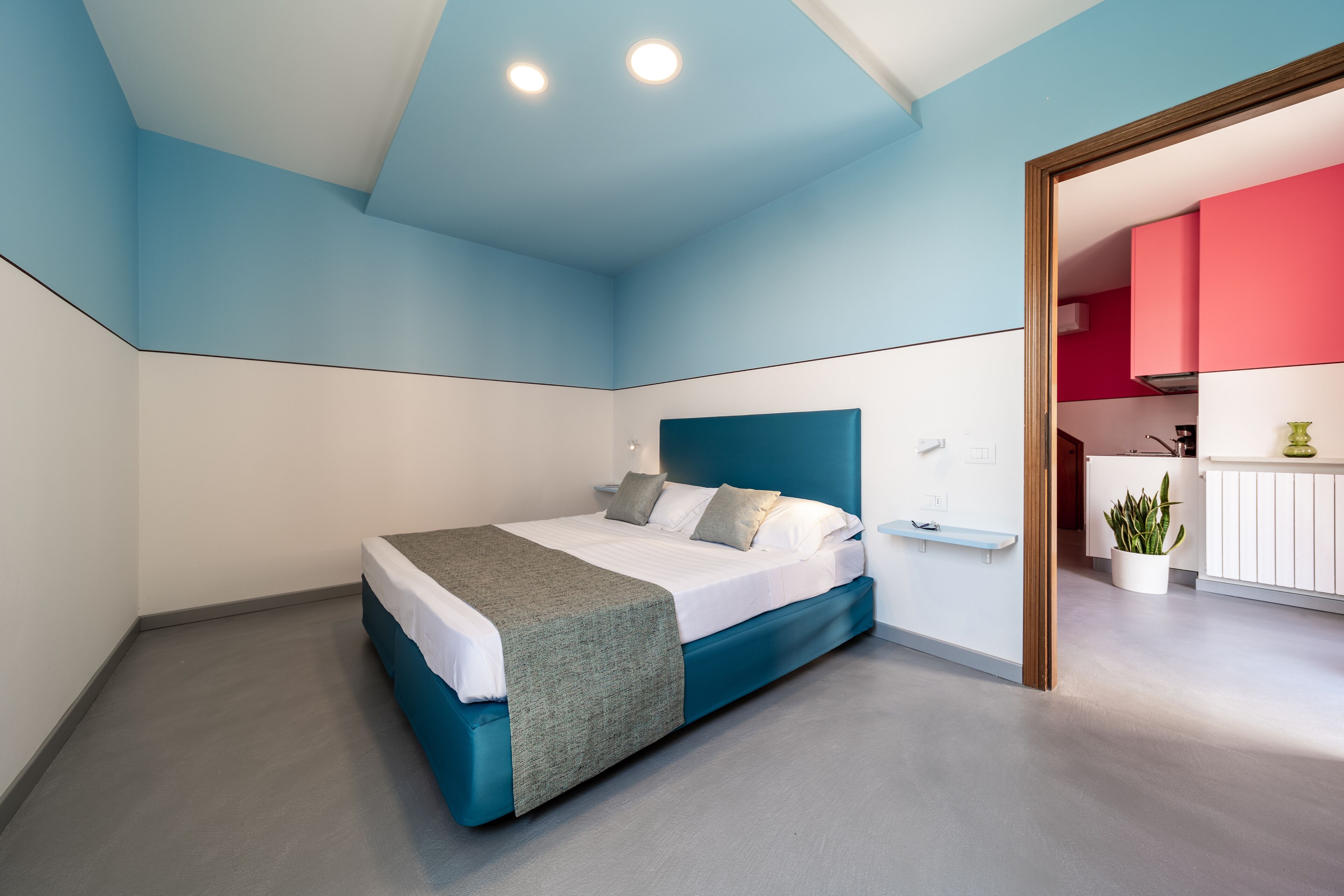 Ein modernes Schlafzimmer mit Bett, Nachttisch und Blick in einen Küchenbereich.