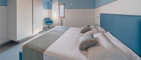 A bedroom with a wooden ceiling, a bed with white bedding, a blue headboard, and a window with curtains.