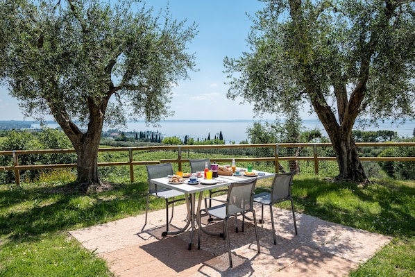 An outdoor dining area with a table set for two, surrounded by chairs, overlooking a scenic view of a body of water and distant cityscape. - Appartamenti Ca' Mure (Bardolino)
