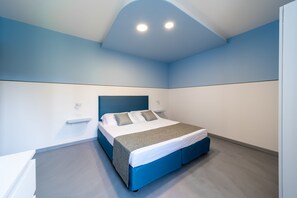 A modern bedroom with a bed, bedside tables, and a blue accent wall. - Appartamenti Ca' Mure (Bardolino)