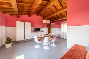 A dining area with a wooden ceiling, a round table with white chairs, and a potted plant. - Appartamenti Ca' Mure (Bardolino)