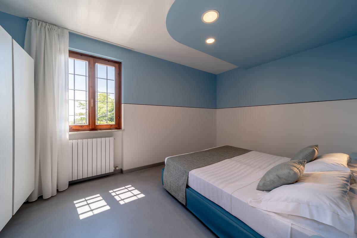 A bedroom with a bed, a window with curtains, and a radiator.