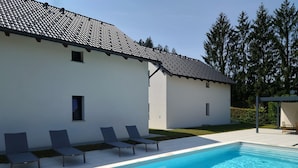 A modern house with a swimming pool, a covered seating area, and a well-maintained lawn.