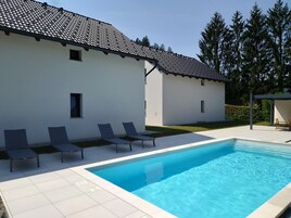 Una casa moderna con piscina, un área de estar techada y un césped bien cuidado.