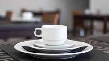 Una taza blanca sobre un platito y un plato, todo dispuesto sobre una mesa con un camino de mesa estampado.