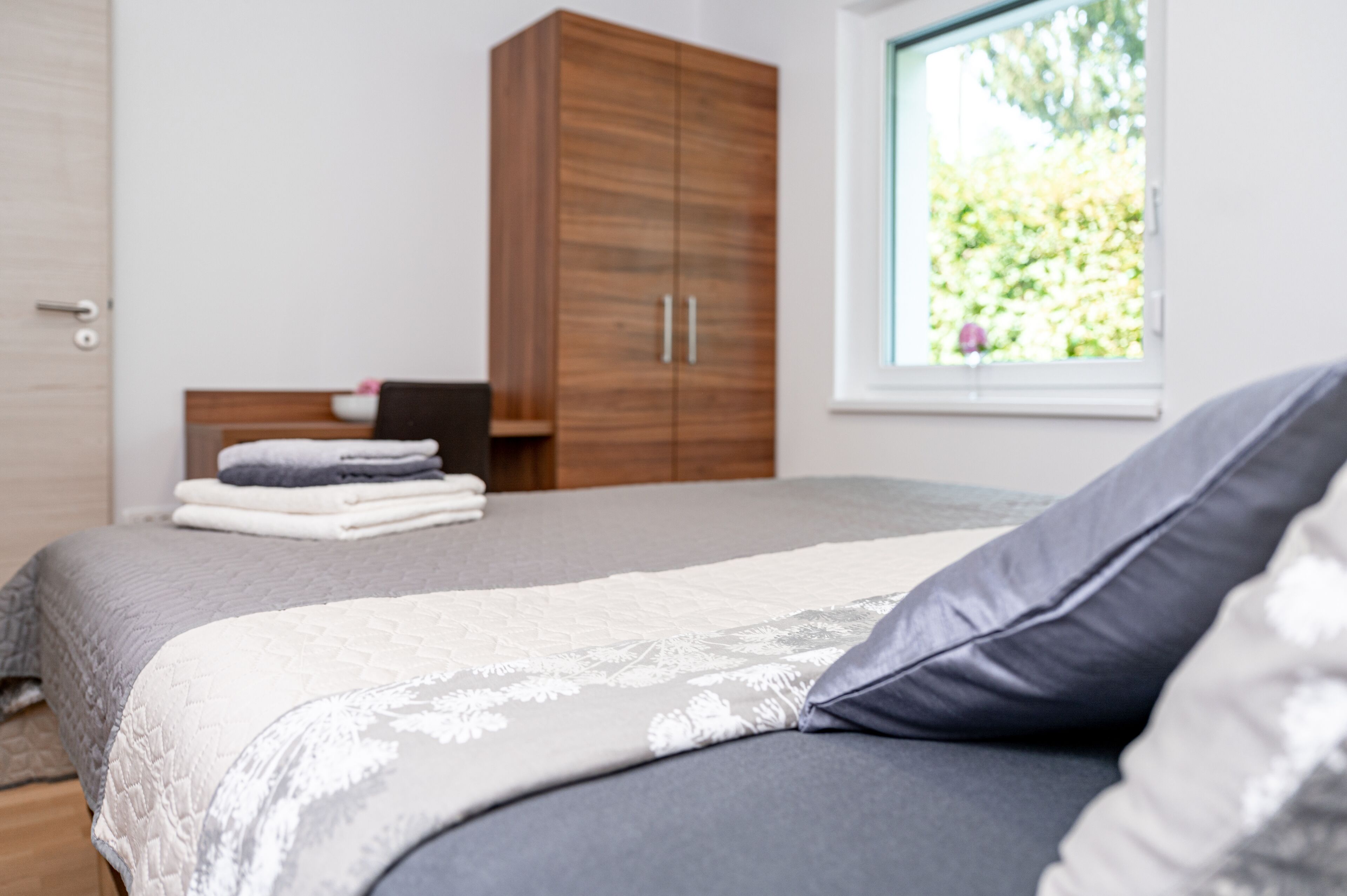 A bedroom with a bed, a wardrobe, and a window with a view of greenery.
