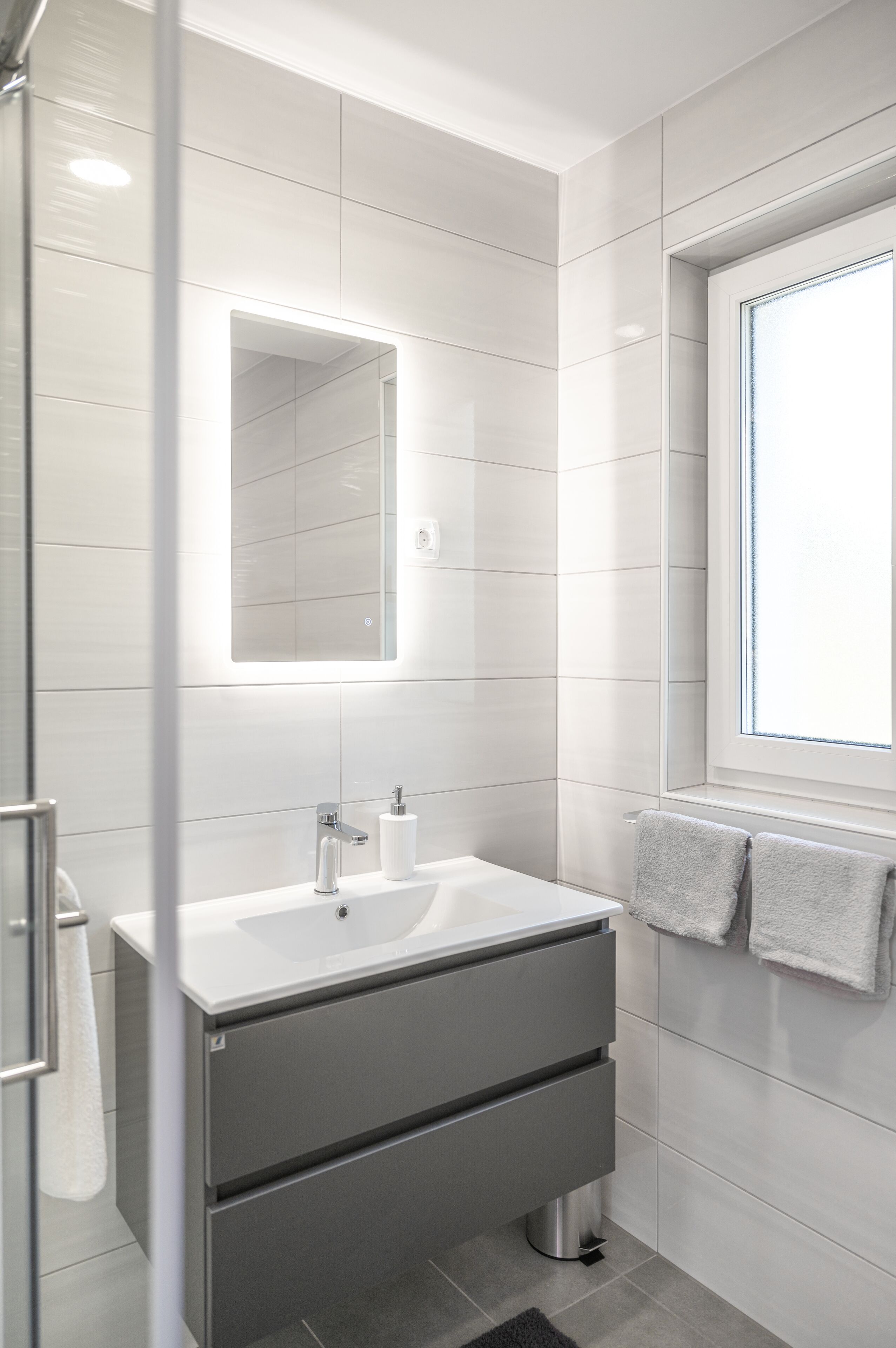 Een moderne badkamer met een wit wastafelmeubel, spiegel en handdoekhouder.