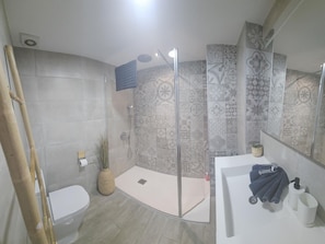 A bathroom with a toilet, a shower with a glass door, a sink with a mirror, and patterned tiles on the walls.
