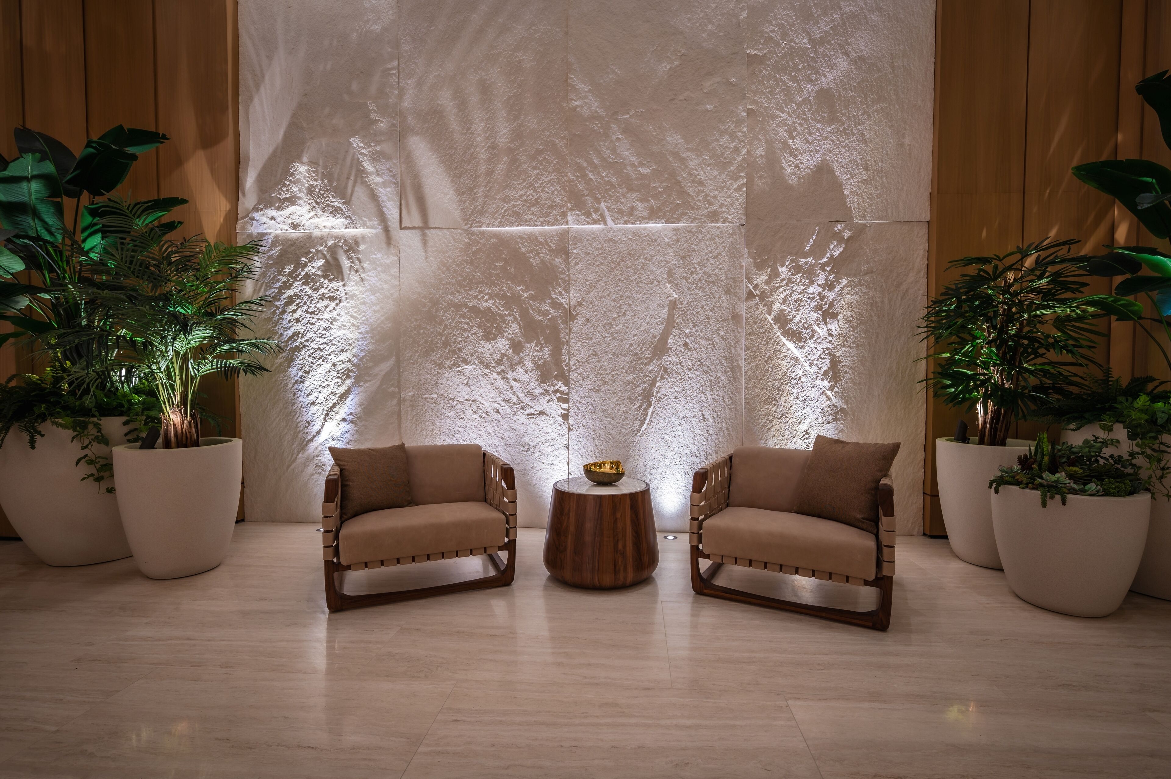A modern room with two leather armchairs, a wooden side table, and large potted plants.