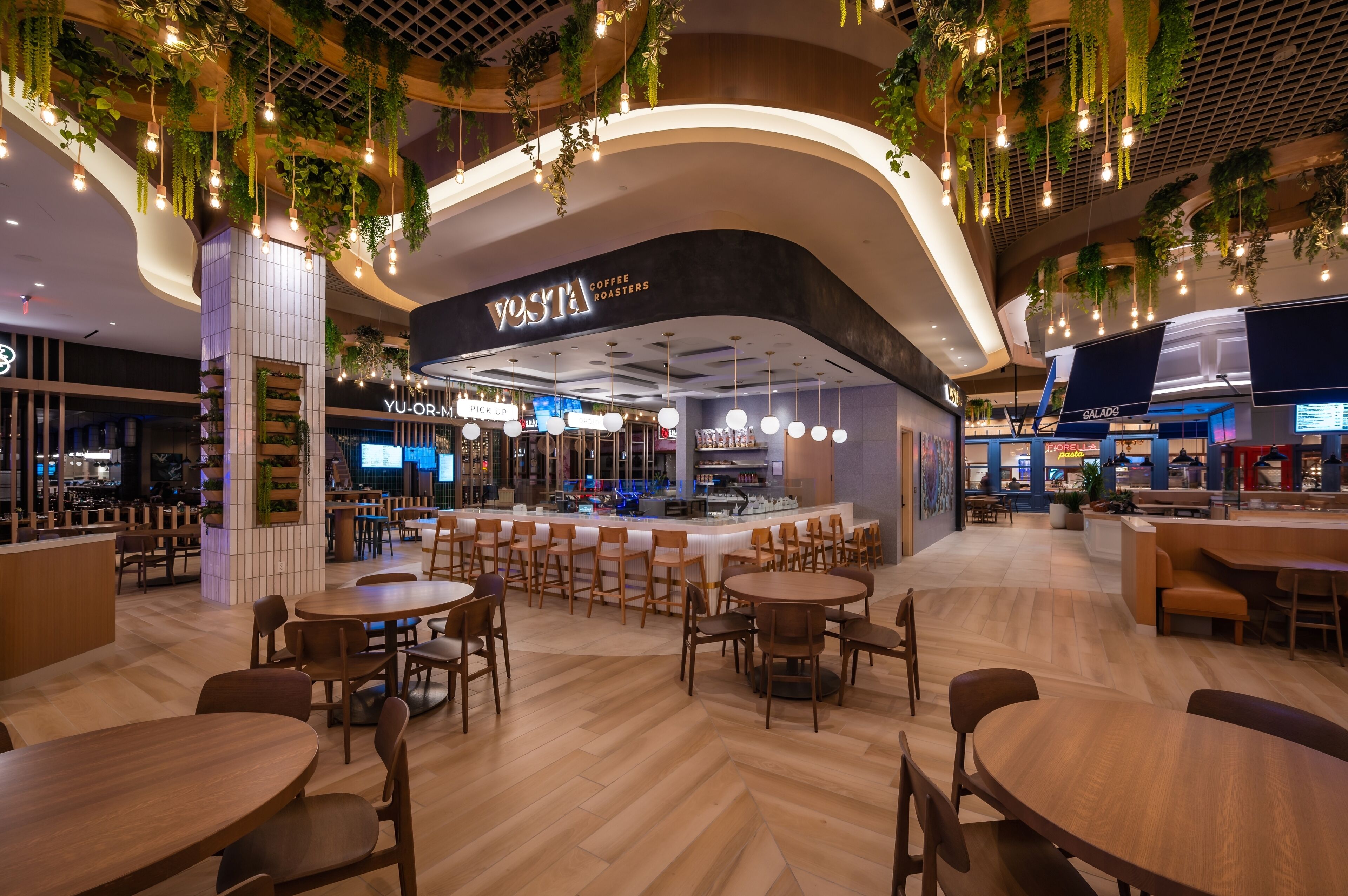 A modern coffee shop with a curved counter, wooden tables, and hanging plants.