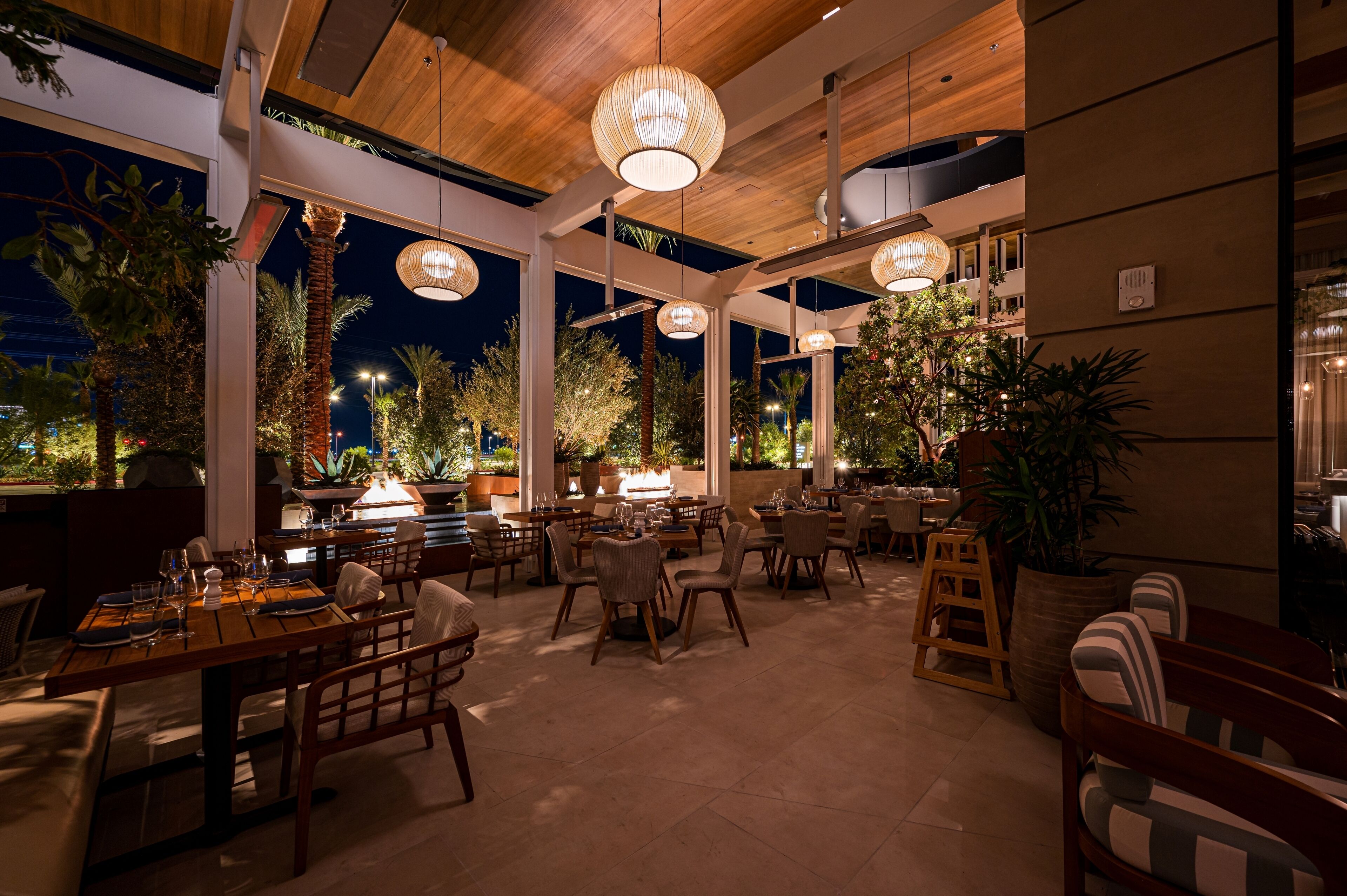 An indoor dining area with tables and chairs, wooden ceiling beams, and hanging pendant lights.
