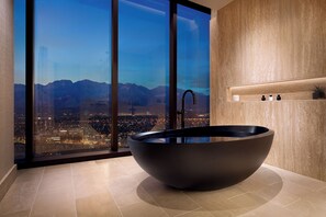 A modern bathroom with a large, dark-colored vessel sink, a glass shower enclosure, and a cityscape view through large windows. - Durango Casino & Resort (Las Vegas)