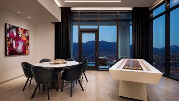 A modern dining area with a table and chairs, a foosball table, and a large window with a cityscape view.