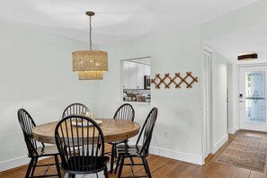 A dining area with a round wooden table and black chairs, a woven pendant light, and a decorative wall piece. - Coastal Paradise Condo (Siesta Key)