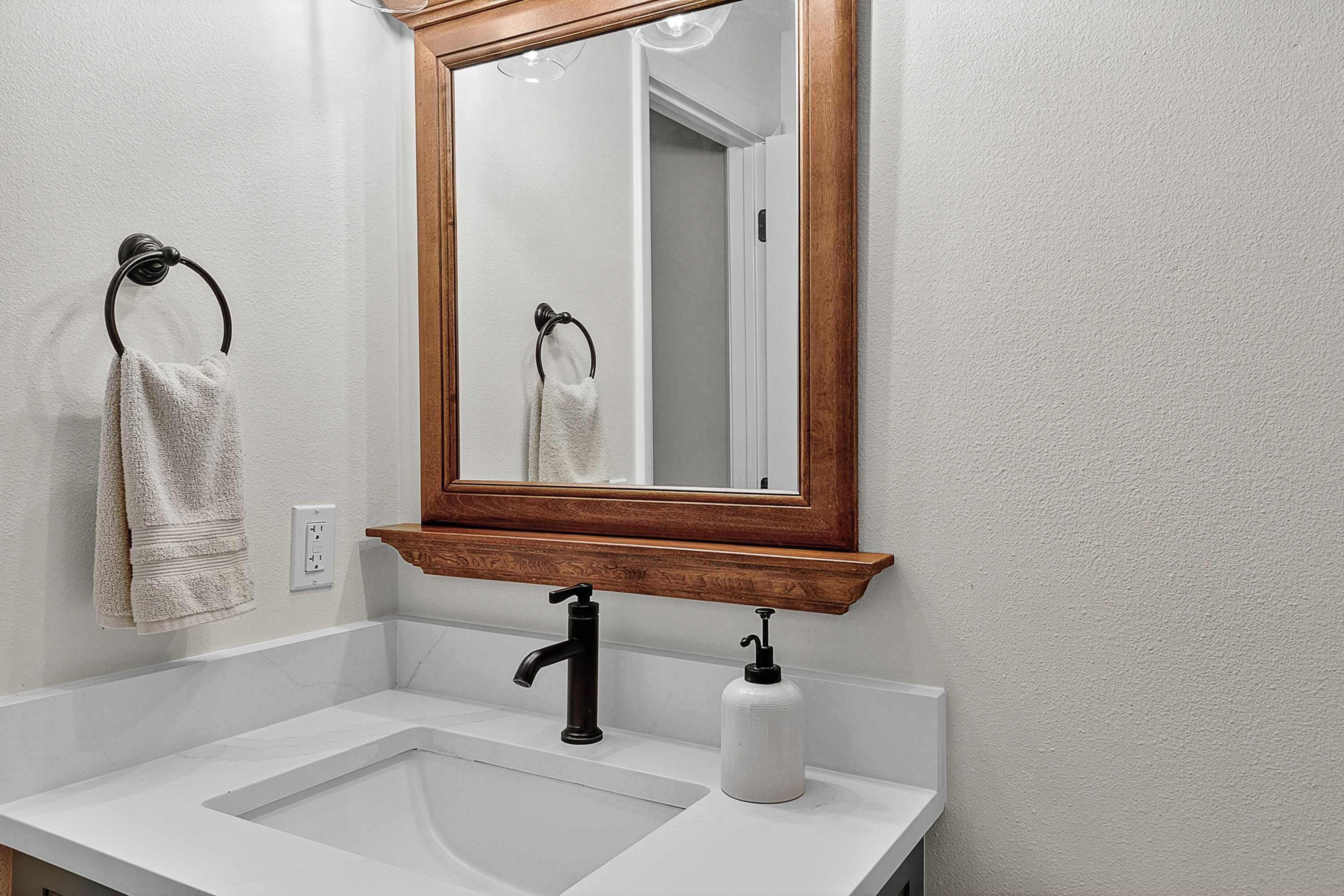 Une salle de bain avec un lavabo blanc, un miroir encadré en bois et un porte-serviette avec une serviette.