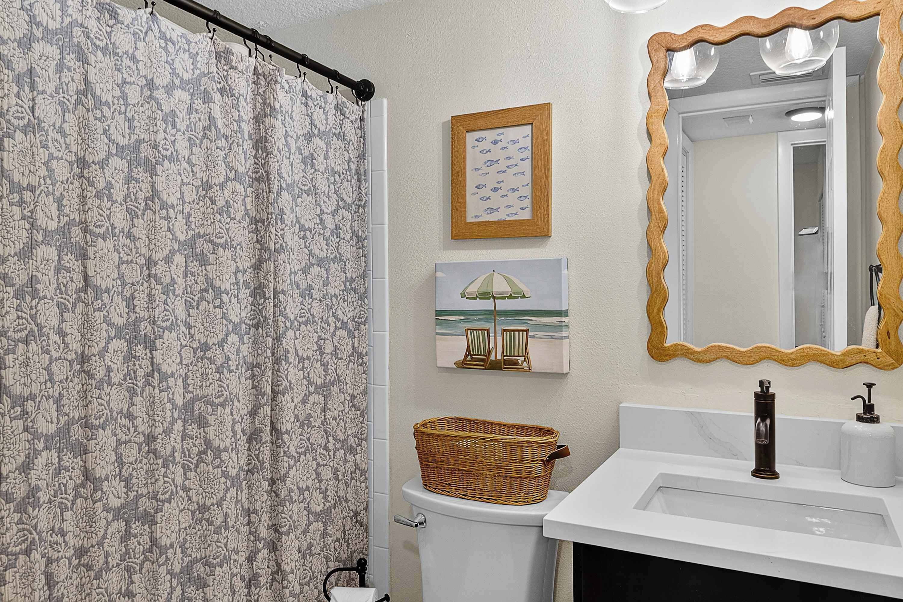 A bathroom with a shower curtain, a toilet, a sink with a mirror, and two framed pictures on the wall.