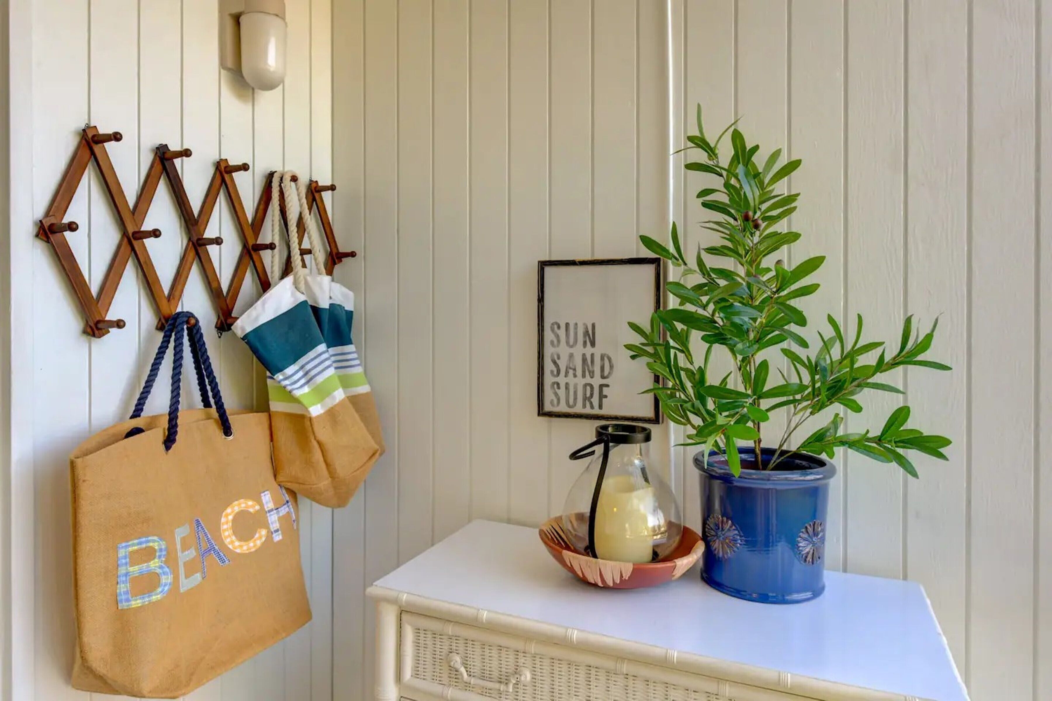 A wall-mounted coat rack with bags, a framed sign, a potted plant, and a small table with a candle and a glass jar.