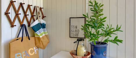 A wall-mounted coat rack with bags, a framed sign, a potted plant, and a small table with a candle and a glass jar.