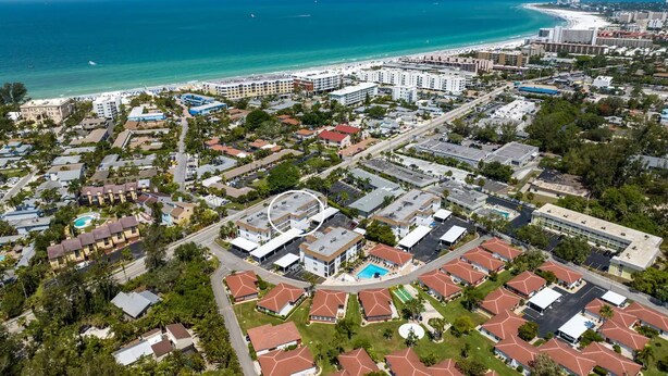An aerial view of a coastal residential area with a beachfront, multi-story buildings, and a swimming pool complex.