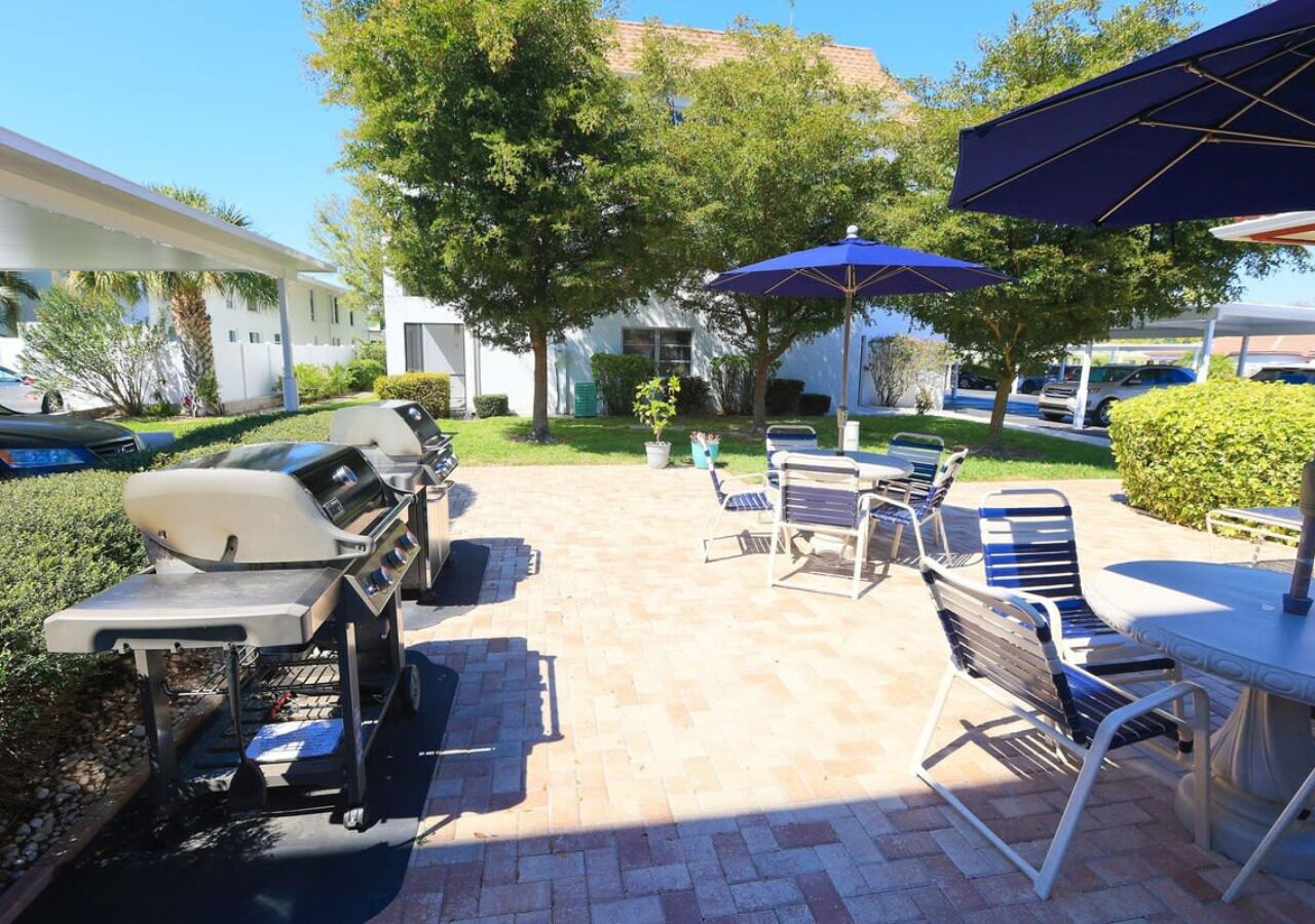 An outdoor patio area with a barbecue grill, seating, and umbrellas.