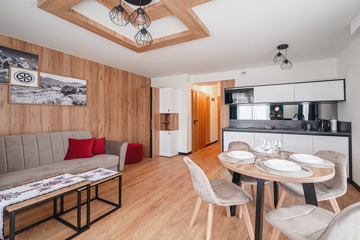 Un salon moderne comprenant un canapé, une table à manger dressée avec des assiettes et des verres, et un coin cuisine avec des placards et un plan de travail.