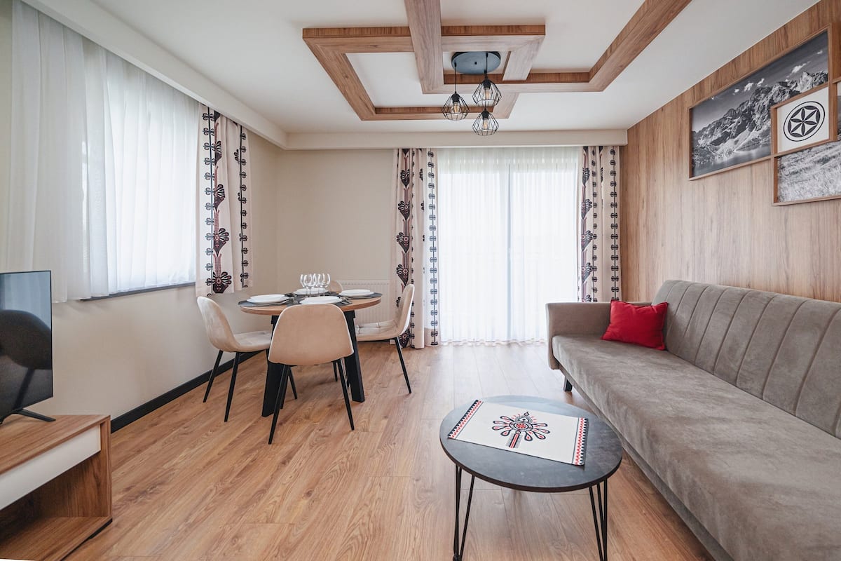 Un salon moderne avec un plafond en bois, un canapé, une table à manger avec des chaises et une petite table d’appoint.
