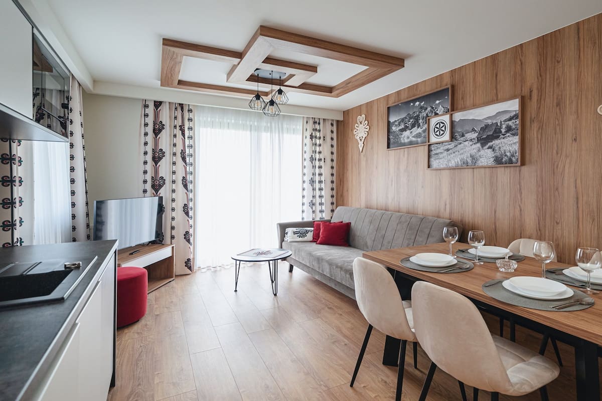 Un espace repas moderne avec une table en bois dressée pour quatre personnes, un canapé gris et un téléviseur en arrière-plan.