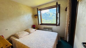 A bedroom with a bed, a window with a mountain view, a radiator, and a small bedside table. - Charming 3-Room Apartment in Châtel - Pets Allowed & Parking (Châtel)