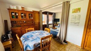 A compact kitchen with wooden cabinets, a dining table with chairs, a coffee maker, and a television. - Charming 3-Room Apartment in Châtel - Pets Allowed & Parking (Châtel)